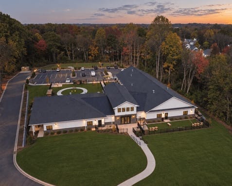 Aerial view of modern residential property with solar panels, manicured lawn, and circular driveway at dusk.