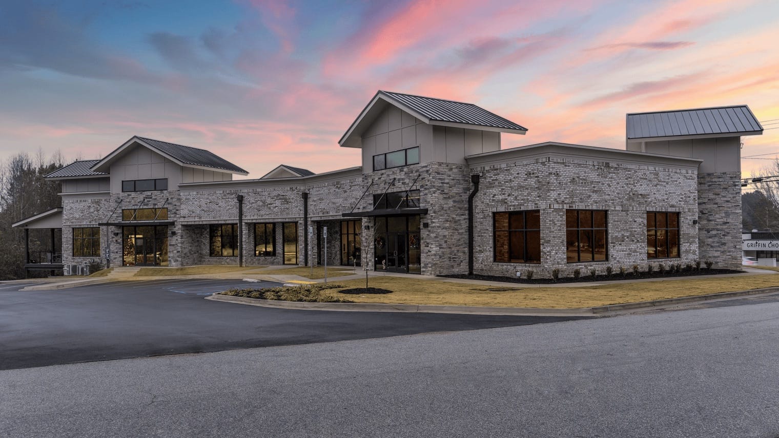 Modern brick commercial building with metal roofs at sunset, featuring large windows and a curved driveway.