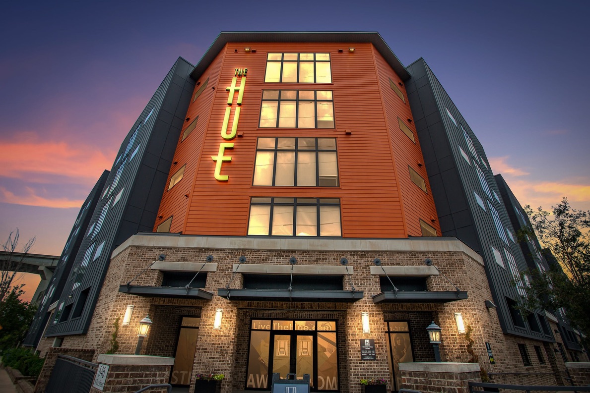Modern brick and metal building with illuminated "THE LOFT" sign at dusk, featuring large windows and entrance doors below.